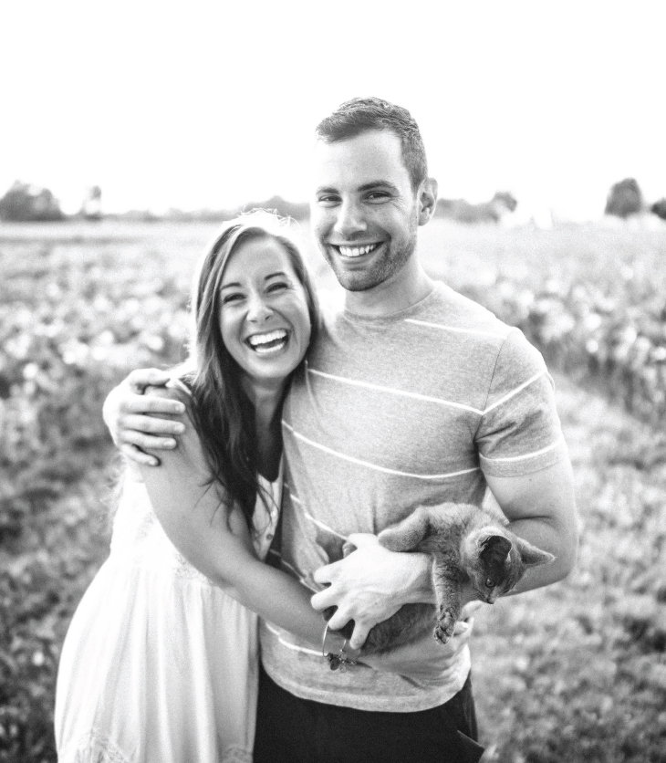 Young couple standing in a field holding their new cat